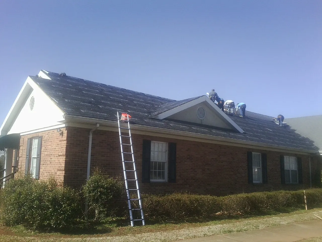 Crew tearing shingles off a brick ranch roof with a ladder set — Emergency Roof Repair work by our crew in Scotland