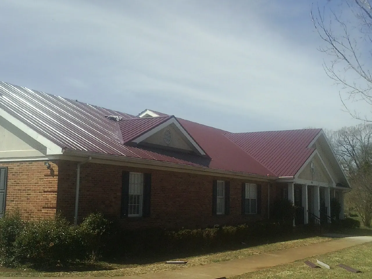 Red metal roof with gabled entries on a long brick building, from a Hail Damage Roof Repair job in Scotland