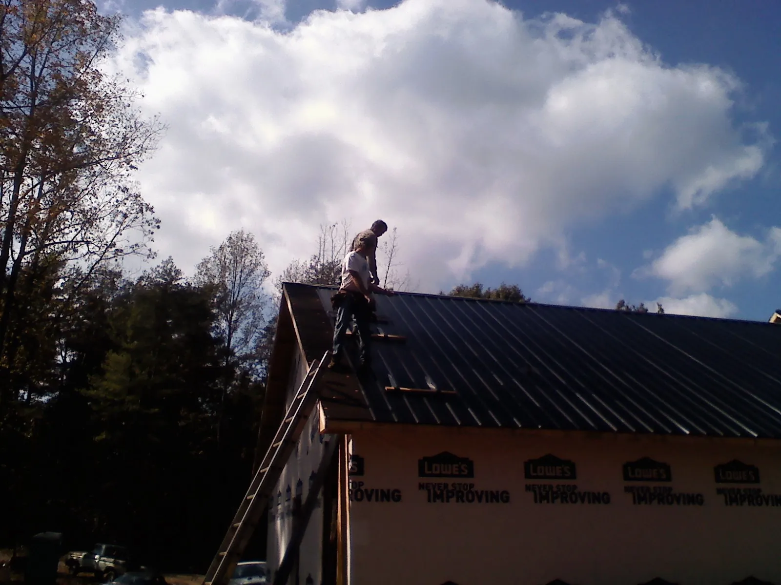 Roofer fastening dark metal panels high against a cloudy sky, from a Roof Inspection job in Scotland